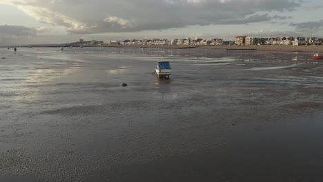 Lonely-boat-on-the-sandy-shore-at-low-tide,-Southend-town-on-on-the-horizon