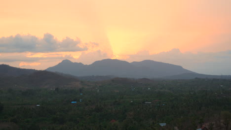 The-sun-sets-behind-a-massive-mountain-range-and-beautiful-scenery-at-the-foot-of-the-mountain-in-Bali