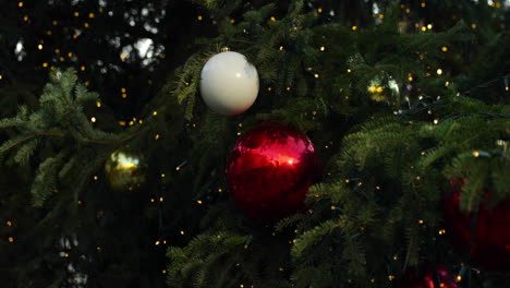 Nahaufnahme-Von-Roten-Und-Weißen-Weihnachtskugeln-Auf-Einem-öffentlichen-Baum,-Der-Tagsüber-Von-Einem-LED-Streifen-Aus-Weihnachtsfichte-Beleuchtet-Wird,-Mit-Starkem-Wind,-Aufgenommen-In-4k-60fps-Zeitlupe
