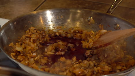 Adding-soy-sauce-to-diced-onions-and-carrots-and-stirring-in-frying-pan,-CLOSEUP