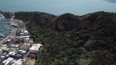 Coastal-City-and-Fishing-Harbor-in-North-Taiwan,-Aerial-View-on-Rainforest-Over-Hills-Near-Yehliu-Geopark-Cape