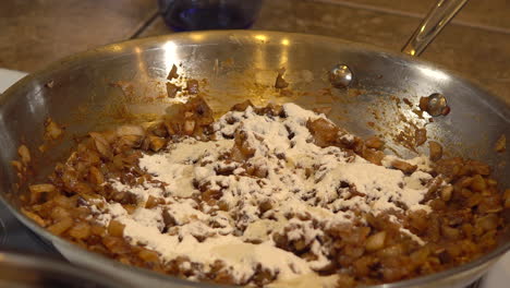Adding-flour-to-brown-ingredients-in-pan-for-recipe-base,-Close-Up