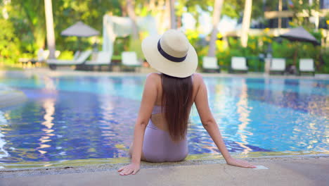 Back-of-Solitary-Fashionable-Woman-Sitting-on-Pool-of-Luxury-Hotel-With-Summer-Hat-and-Swimsuit,-Static-Shot