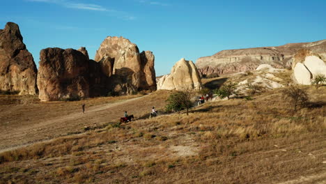 Tourists-on-Horseback-riding-into-Sunset-over-hills-of-Goreme,-Cappadocia
