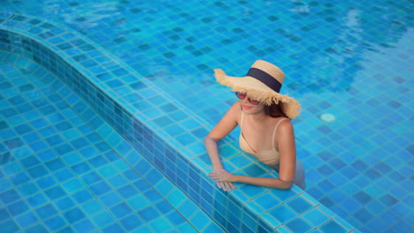 Solitary-Stylish-Asian-Woman-in-Hotel-Pool-With-Summer-Hat-and-Sungrasses,-Luxury-Summer-Vacation-Concept