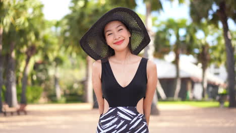 Beautiful-young-woman,-wearing-a-black-floppy-hat,-looking-directly-into-the-camera-and-smiling