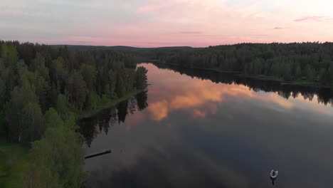 Drone-aerial-flight-over-calm-lake-inside-forest-in-the-wilderness-in-Scandinavia-during-sunset