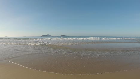 Low-angle-seascape-at-the-Atlantic-shore-with-clear-water-waves-coming-in-at-sunrise-with-the-islands-just-outside-of-Ipanema-beach-in-Rio-de-Janeiro-on-the-horizon
