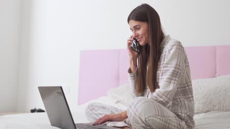 pretty-girl-in-pajamas-in-bed-talking-on-the-phone-and-working-on-a-laptop