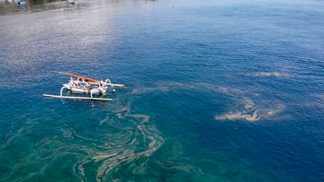 Aerial-over-local-fishing-canoe-in-Amed,-Bali,-Indonesia-fishing-in-heavily-polluted-waters