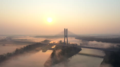 Aerial-shot-over-a-wide,-calm-river,-during-a-foggy-morning,-towards-a-modern-cable-road-bridge