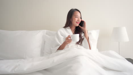 Asian-lady-having-comfy-cozy-time-on-a-hotel-bed-answering-a-phone-call