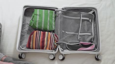 girl-collects-a-suitcase-for-vacation,-closeup-top-view