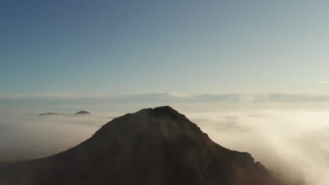 Fog-Swirling-Around-Silhouette-Mountain,-Aerial-Birds-Eye-View-Above-Clouds