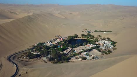 Aerial,-drone-shot,-overlooking-the-Huacachina-oasis-village,-on-a-partly-sunny-day,-in-southwestern-Peru