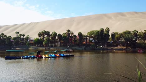 Aerial,-drone-shot,-towards-pedalo-boats,-on-the-Huacachina-lagoon,-the-oasis-village,-on-a-sunny-day,-in-south-Peru