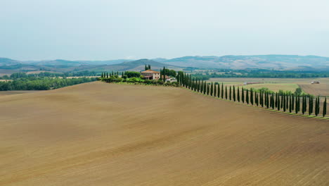 Tuscany-landscape-with-cypress-driveway-leading-to-traditional-Vila,-Aerial-pan