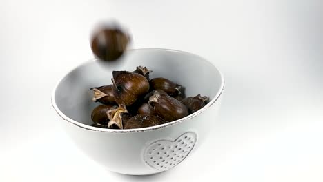 Roasted-chestnuts-falling-into-white-ceramic-bowl,-STILL,-SLOMO,-ISOLATED