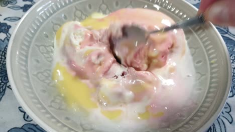 Strawberry,-vanilla-and-black-current-flavored-ice-cream-with-yellow-vanilla-custard-topping,-delicious-sunday-dessert-being-scooped-with-stainless-steel-spoon-in-porcelain-bowl