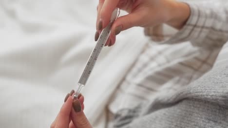 Close-up-scene-of-a-girl-who-is-lying-in-the-bed-and-holding-a-mercury-thermometer-in-her-hand