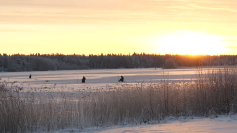 Ice-fisherman-on-a-beautiful-frozen-snow-covered-lake-at-sunrise