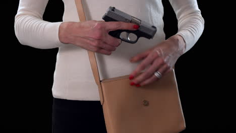 Woman-pulling-concealed-handgun-from-purse-for-personal-protection-with-black-background