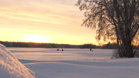 Winter-landscape-covered-with-fresh-powder-and-people-in-horizon-during-sunset,-Slow-pan-left