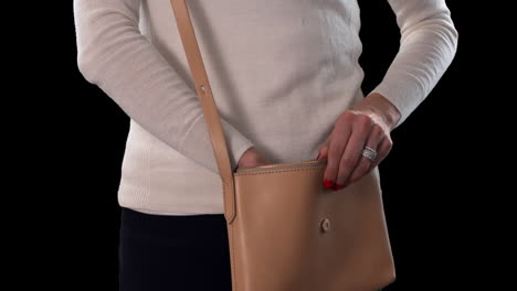 Woman-tries-to-remove-handgun-from-purse-slowly-to-keep-it-concealed-with-black-background