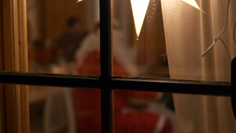 X-mas-background-seen-through-window,-defocused-Santa-Claus-handing-out-gifts-at-Christmas-celebration-party