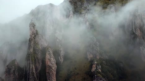Aerial,-rising,-drone-shot-towards-rocky-peaks-and-fog,-in-the-Andes-mountains,-on-a-cloudy-day,-near-Cusco,-in-Peru,-South-America