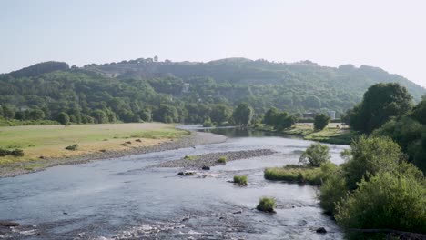 Scenic-landscape-of-River-Wye-gliding-through-stone-banks,-green-hill-as-background-Builth-Wells,-Wales-Uk