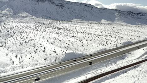 Highway-through-snow-covered-mountainside,-aerial-side-truck-view