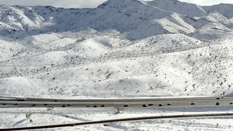 Aerial-view-tracking-right-across-highway-traffic-in-winter-snowy-mountain-landscape-scene