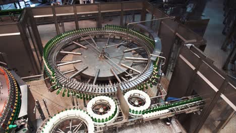 Green-glass-bottles-being-processed-on-circle-conveyor-inside-brewery-factory