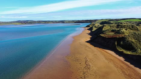 Aerial-flying-over-ocean-at-Tramore-Beach,-Ireland-during-the-day,-calm-sea