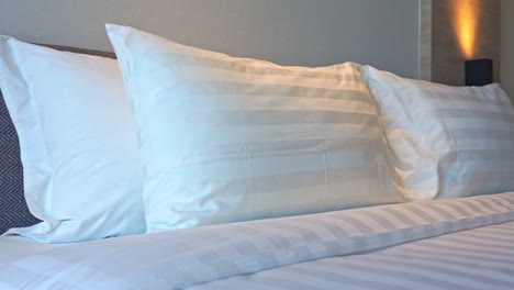 Pan-of-luxury-hotel-bed-with-striped-white-duvet-and-pillows,-medium-shot