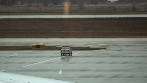 A-car-drives-on-the-airport-apron-while-another-one-is-parked-nearby-with-lights-flashing-on-top