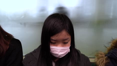 Im-öffentlichen-Zug-In-Tokio,-Japan-Sitzt-Ein-Junges-Mädchen-Mit-Einer-Schützenden-Gesichtsmaske---Nahaufnahme