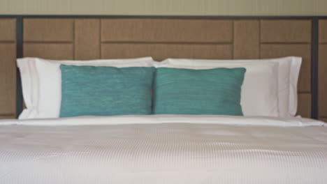 Tilt-up-of-a-luxurious-bed-in-the-room-of-a-resort-with-white-duvet-and-aqua-pillows