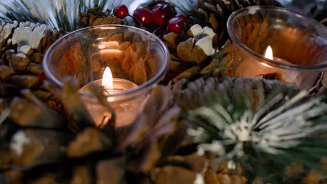 Close-up-shot-of-two-burning-tea-lights-in-a-Christmas-decoration-of-fir-cones