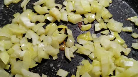 Close-up-of-fresh,-white-onion-that-has-been-chopped-up-and-put-into-a-black-pan-to-fry,-slowly-heating-up