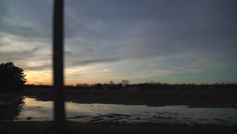 Blick-Aus-Dem-Seitenfenster-Des-Autos,-Während-Sie-Bei-Friedlichem-Sonnenuntergang-Am-Farmland-Vorbeifahren