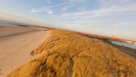 Fast-drone-shot-flying-low-above-the-dunes-towards-a-touristic-town-during-winter