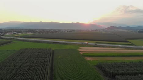 Fields,-Cars-on-Highway,-Distant-Mountains,-Sunset,-Establisher-AERIAL