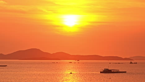 Tropischer-Orangefarbener-Sonnenuntergang,-Der-Sich-Auf-Dem-Wasser-Mit-Hügeln-Und-Fischerbooten-Widerspiegelt