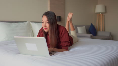 Young-woman-lying-on-the-bed-working-on-her-laptop