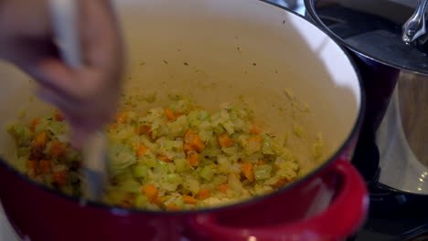 Hand-Stirring-Chopped-Carrots-and-Onions-in-Pot,-Closeup