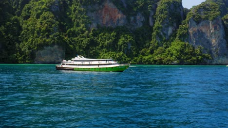 Green-and-white-ferry-boat-anchors-at-deep-blue-sea-at-Ko-Phi-Phi-island-in-Thailand