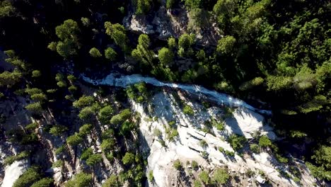 Drone-Aerial-View-of-Snowmelt-Water-in-Mountainous-Stream-and-Waterfall-in-Evergreen-Forest-in-Sequoia-National-Park,-Under-Mount-Whitney,-California-USA