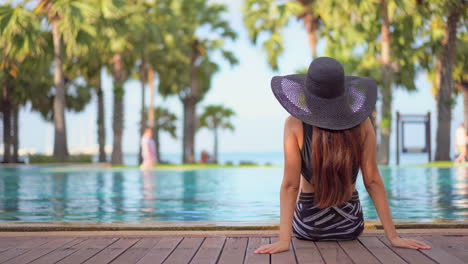 Fashionable-woman-sitting-by-the-pool-in-tropical-holiday-scenery